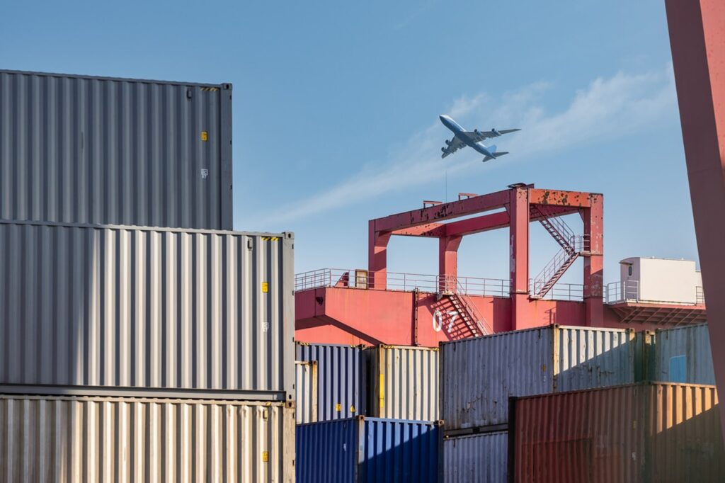 container-yard-closeup-with-airplane-in-sky-2023-11-27-04-50-06-utc.jpg